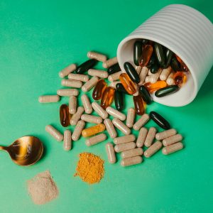 A mix of capsules, pills, and powder on green background with spoon.