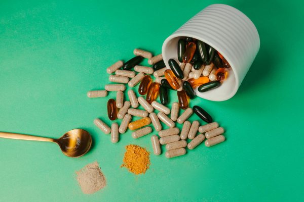 A mix of capsules, pills, and powder on green background with spoon.