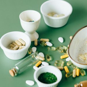 Assorted natural supplements and pills in ceramic bowls on a green background, showcasing health and wellness themes.