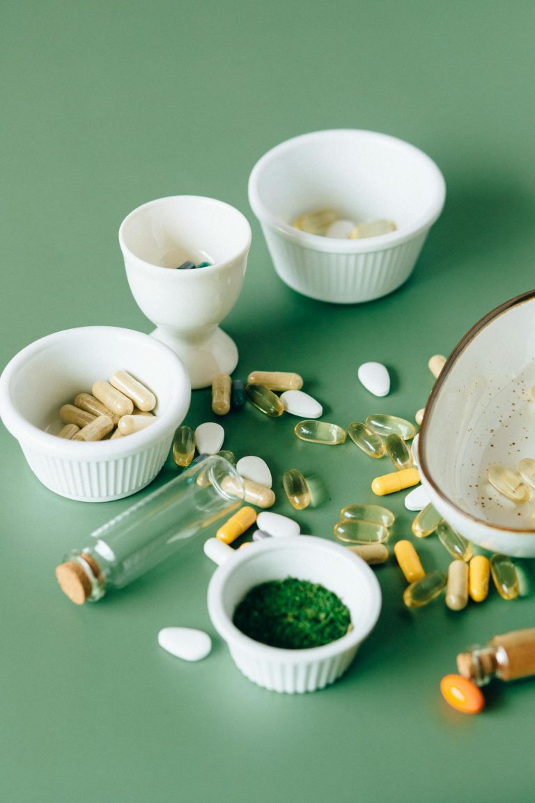 Assorted natural supplements and pills in ceramic bowls on a green background, showcasing health and wellness themes.