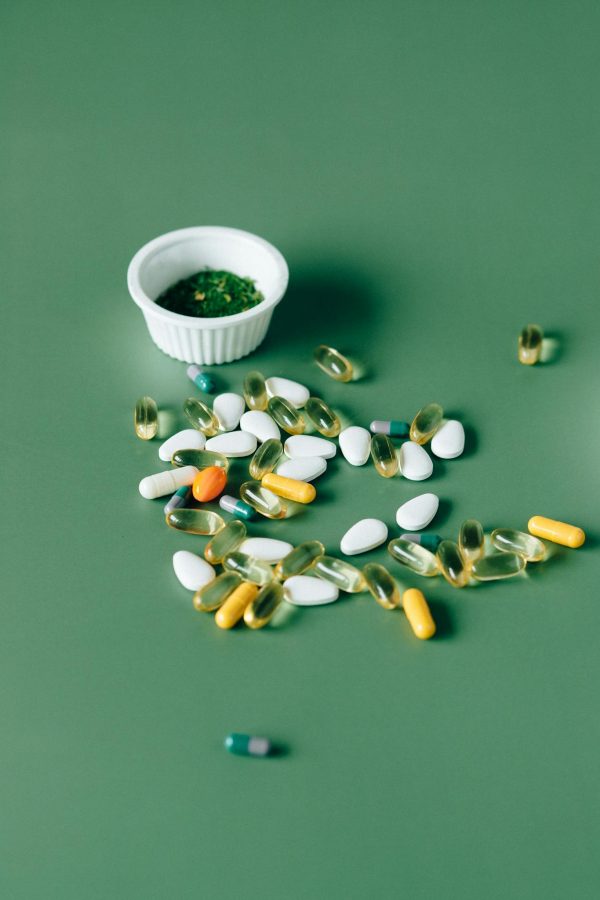 Assorted pills and herbal remedies displayed on green surface, emphasizing natural health concepts.