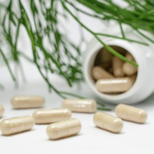 Close-up of herbal capsules spilling from a bottle with green plants in the background.