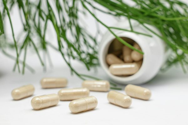 Close-up of herbal capsules spilling from a bottle with green plants in the background.