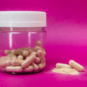 Jar of brown capsules and powder on a vibrant pink backdrop.