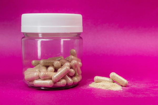 Jar of brown capsules and powder on a vibrant pink backdrop.