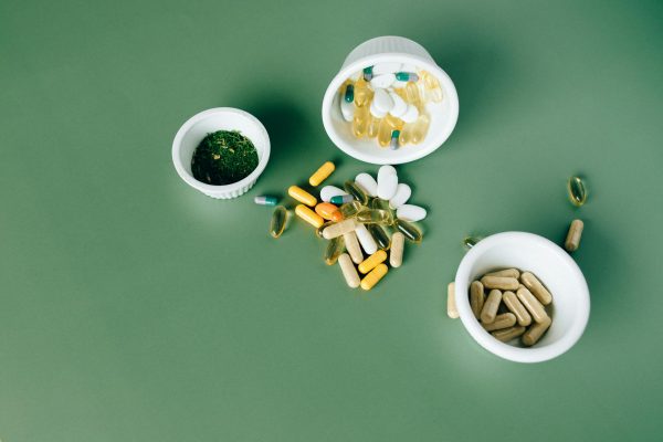 Various herbal and vitamin pills and capsules on a green surface.