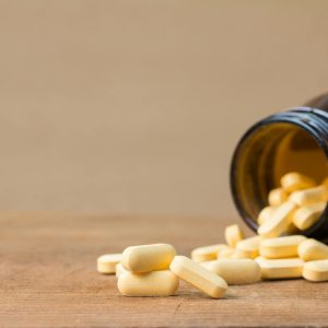 Yellow pills spill from a brown bottle onto a wooden surface, showcasing a health or medicine concept.