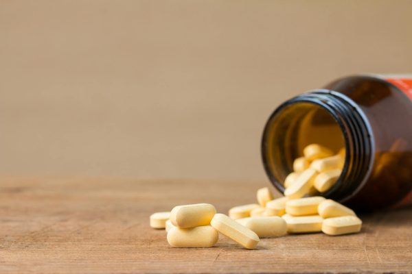 Yellow pills spill from a brown bottle onto a wooden surface, showcasing a health or medicine concept.